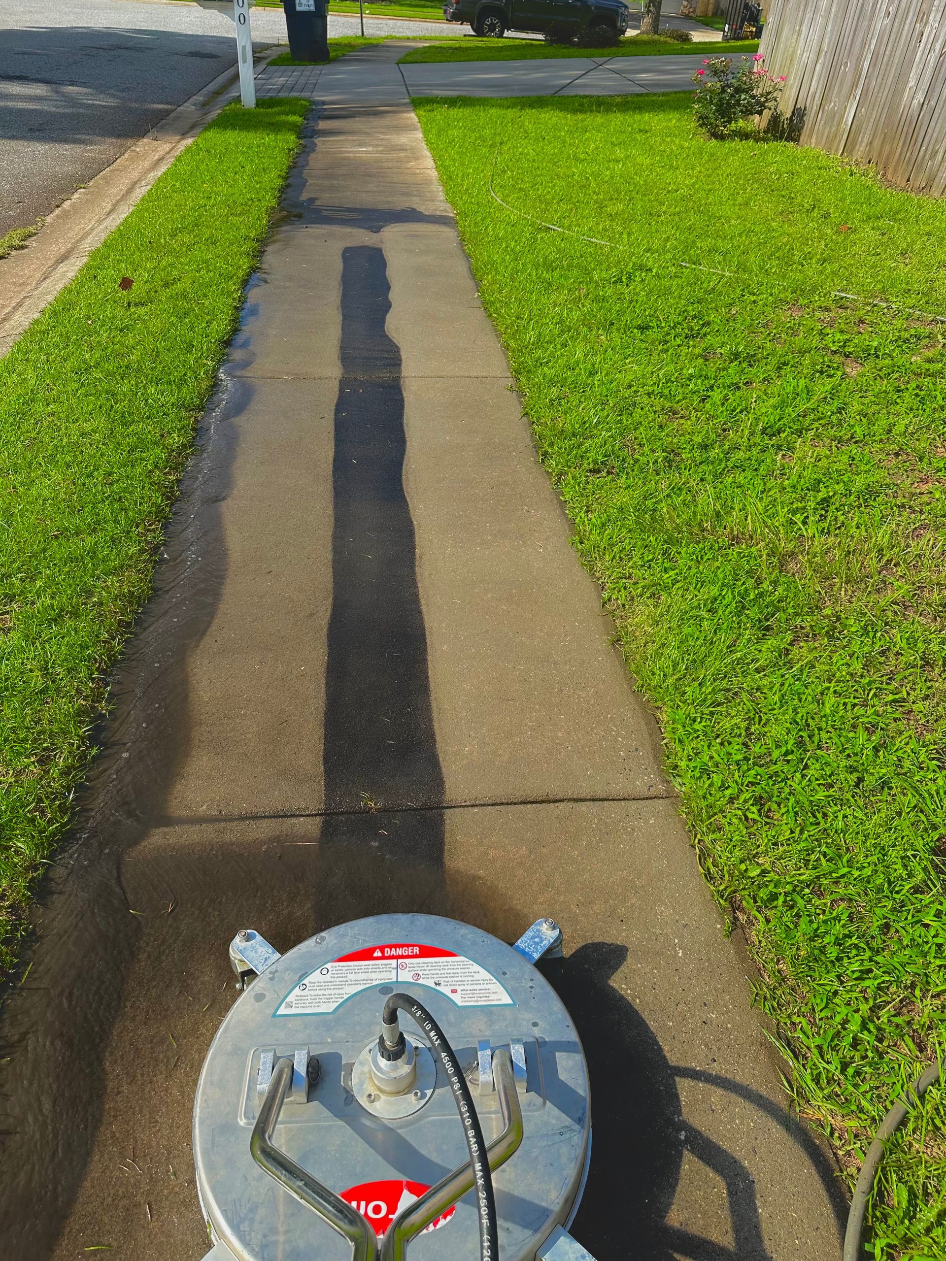 A man is using a high pressure washer to clean a cobblestone driveway.