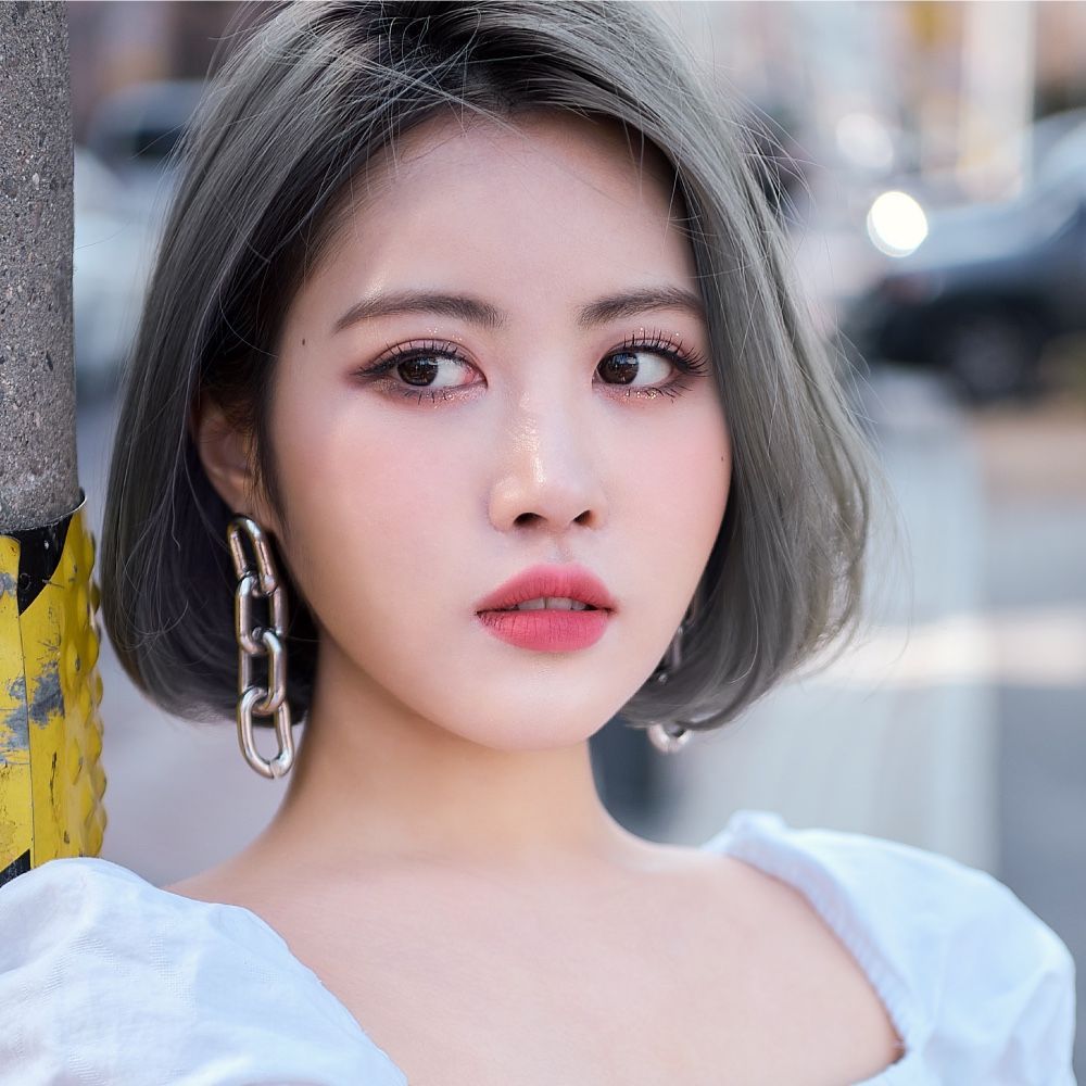 Portrait of a woman with a short gray bob, white top, and large earrings on a city street