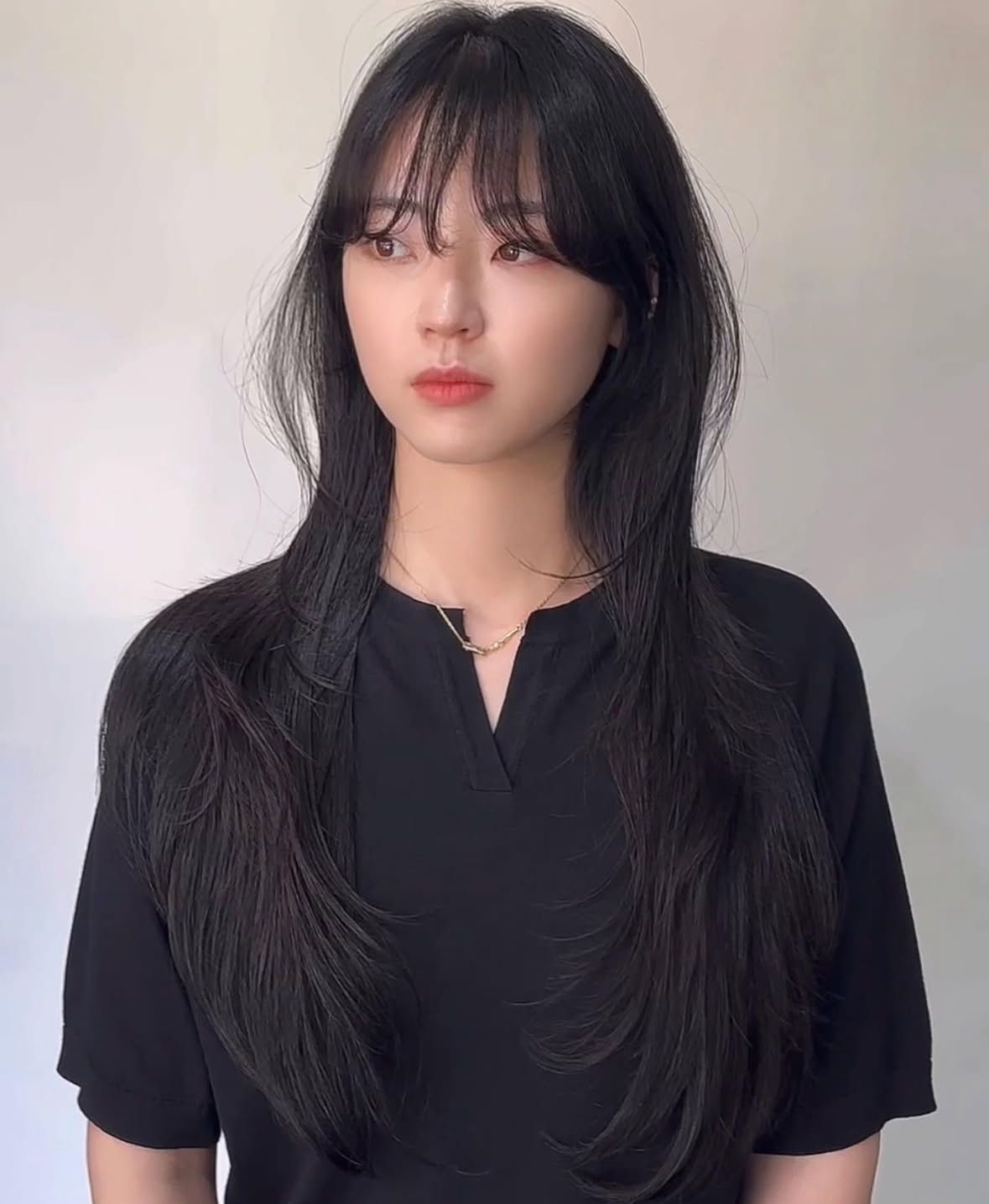 Portrait of a woman with long black hair wearing a black top against a light background