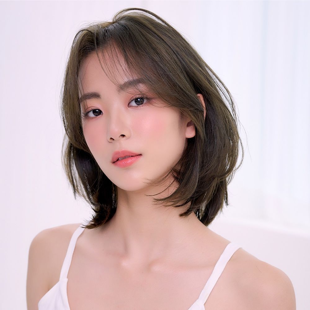 Portrait of a woman with short dark hair and pink makeup against a light background