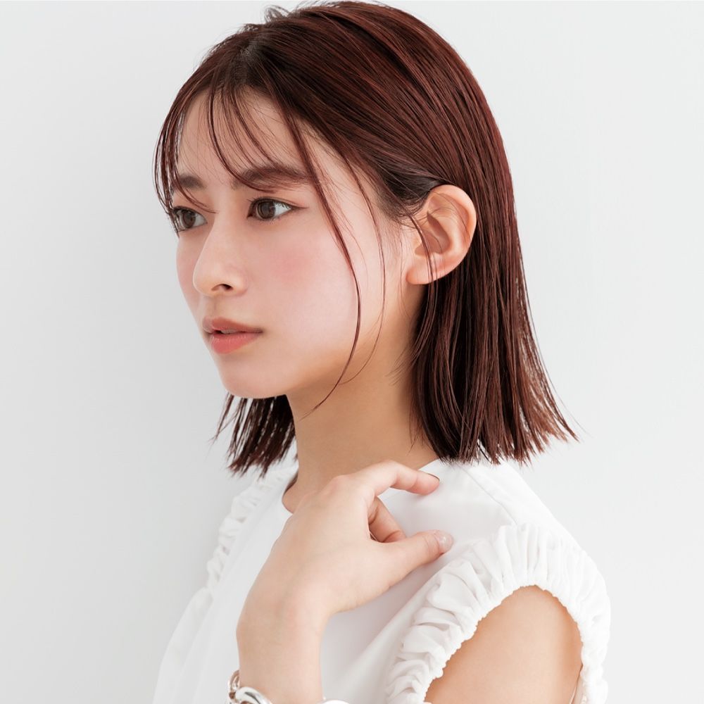 Side-profile portrait of a woman with short auburn hair in a white top against a white background
