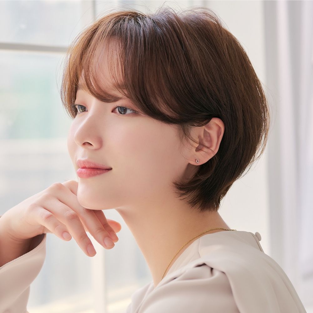 Person with short brown hair resting chin on hand by a bright window