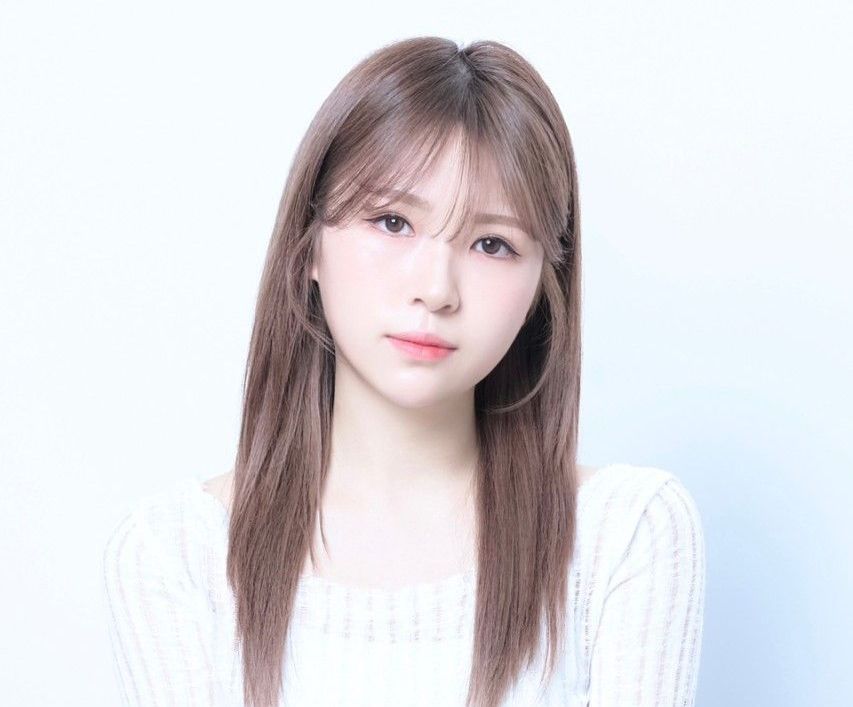 Portrait of a young woman with long brown hair in a white sweater against a soft blue background