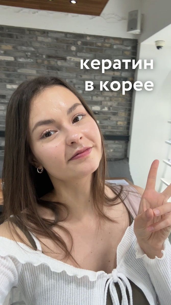 Woman in white top taking a selfie indoors, making a peace sign, with “кератин в корее” text overlay