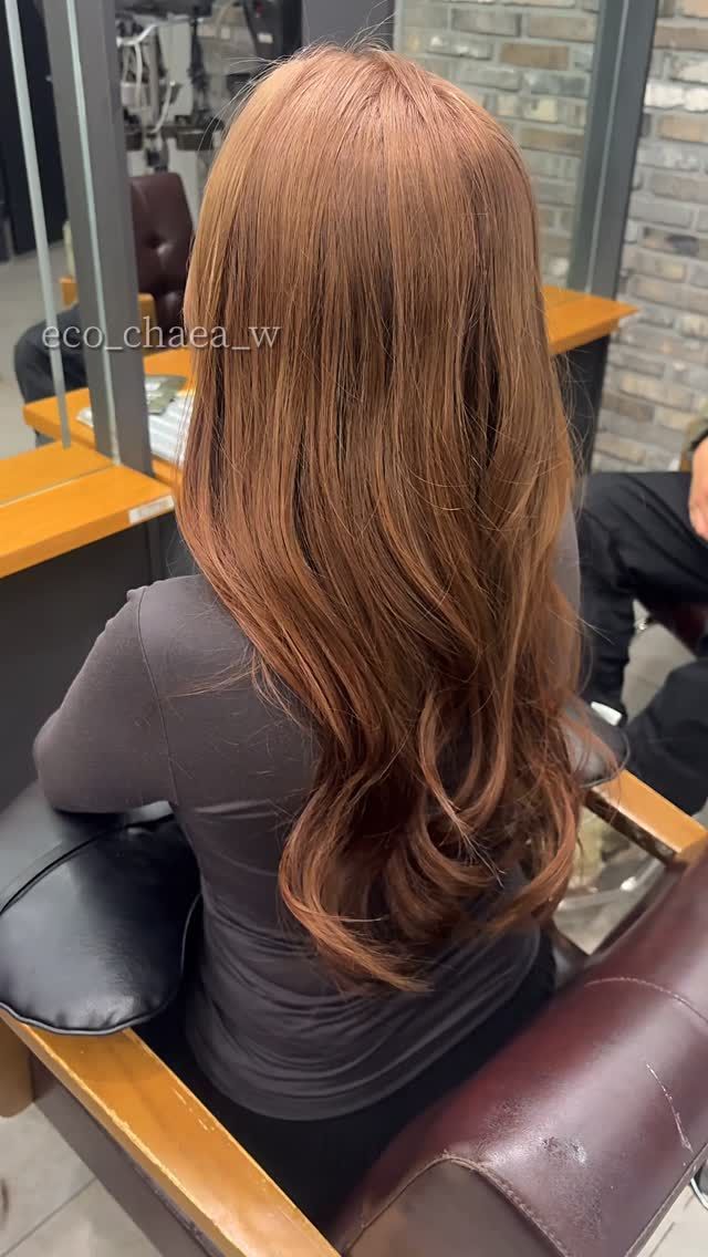 Long wavy brown hair seen from behind in a salon chair, with a glossy finish.