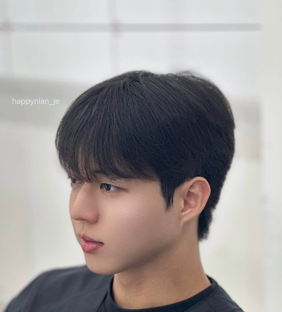 Side-profile portrait of a person with dark hair, looking left in a soft, bright indoor setting.