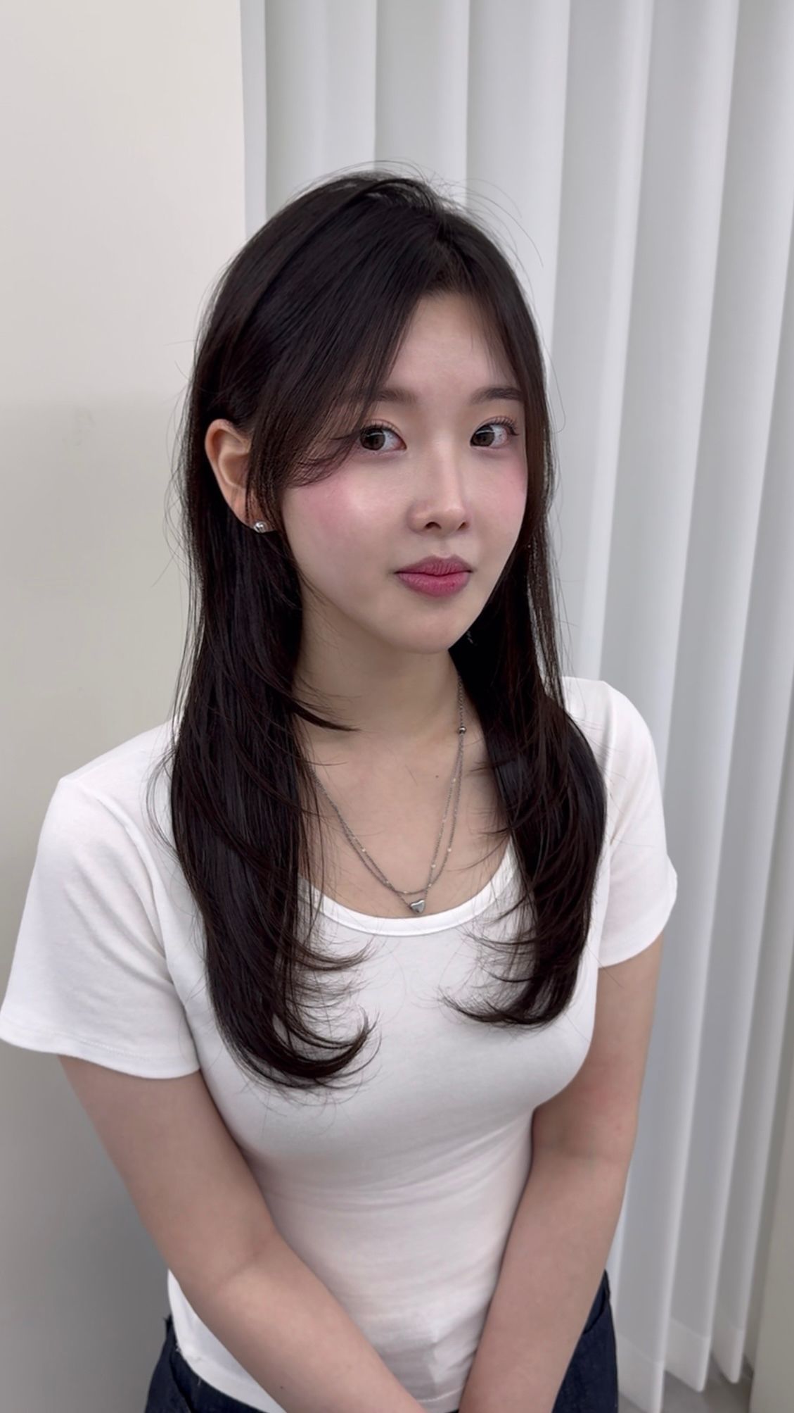 Portrait of a woman in a white top standing before light curtains, looking at the camera with a slight smile