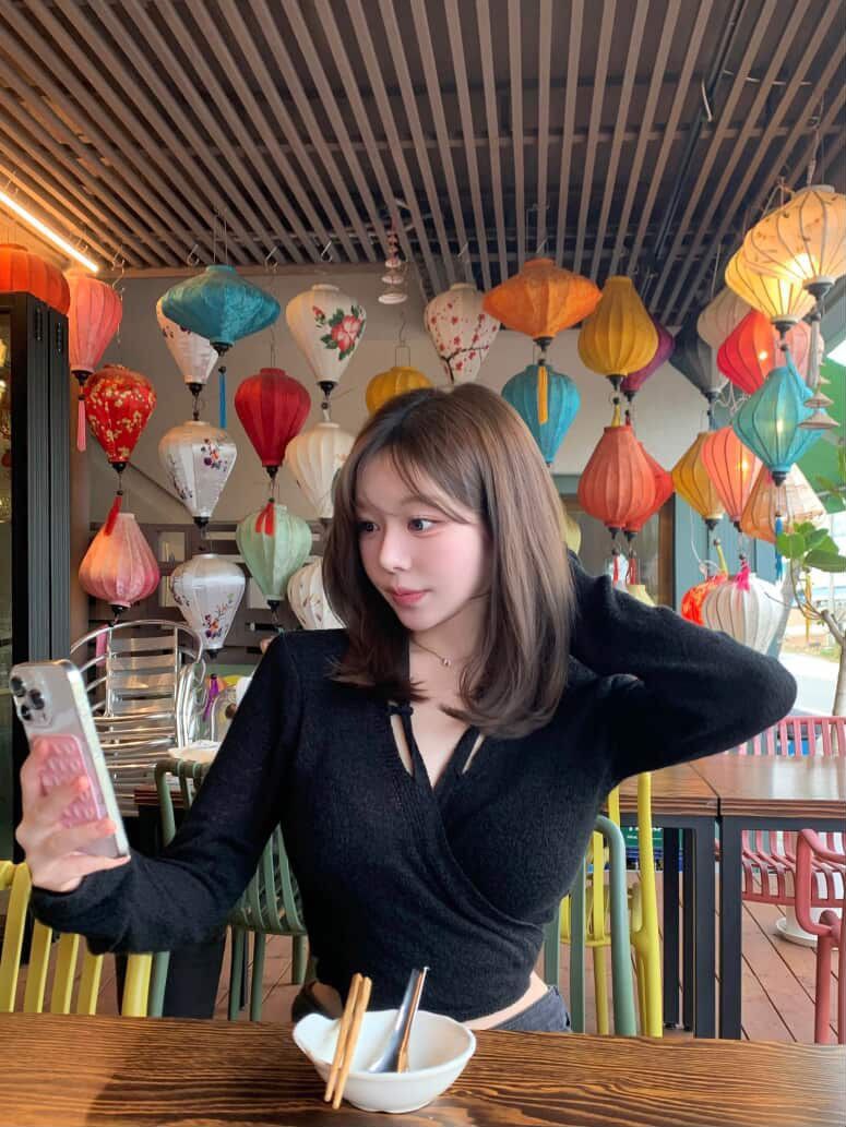 Woman in a black top holding a drink in a colorful restaurant decorated with hanging lanterns