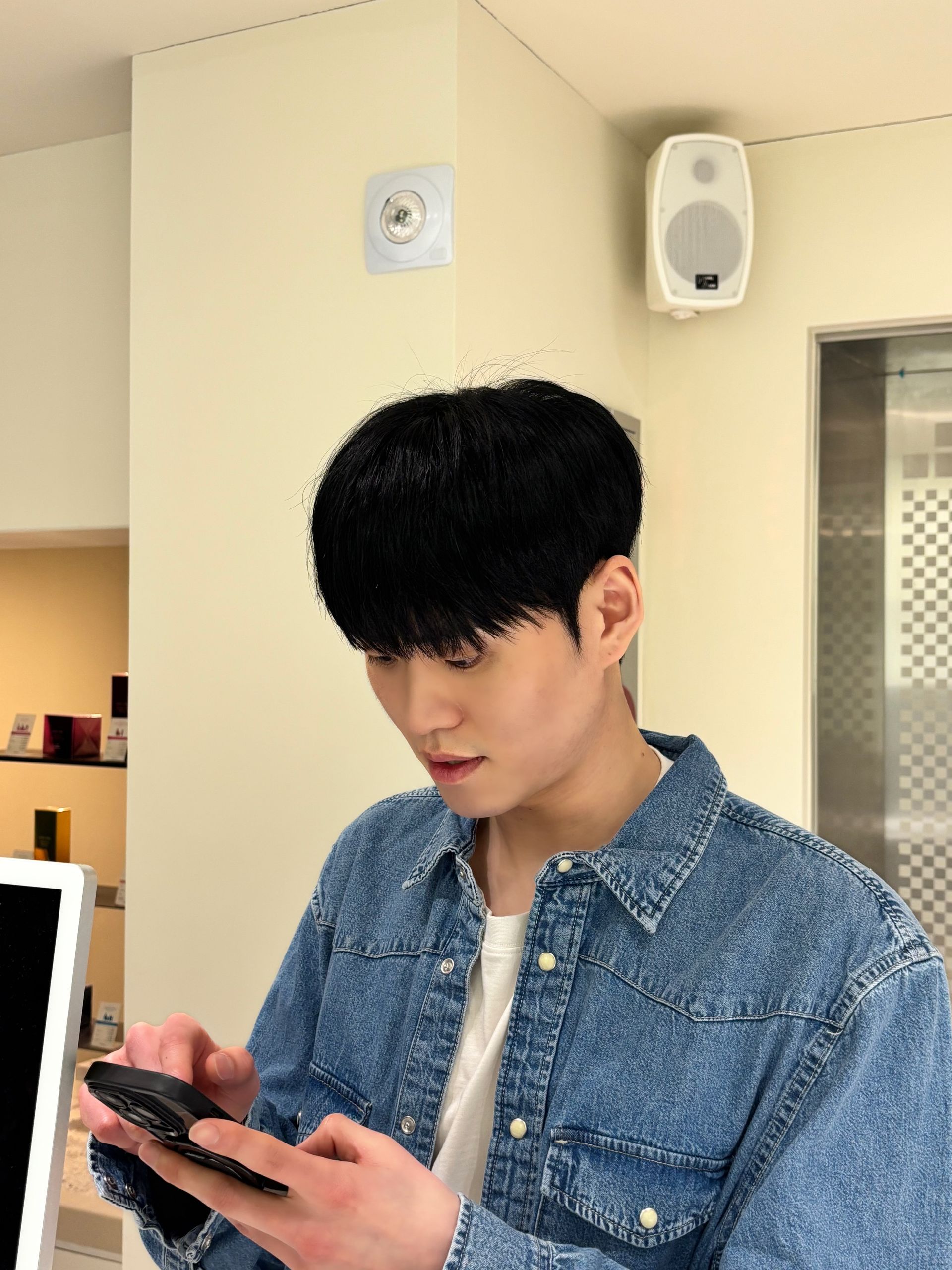 Person in a denim jacket looking at a phone in a bright indoor room.