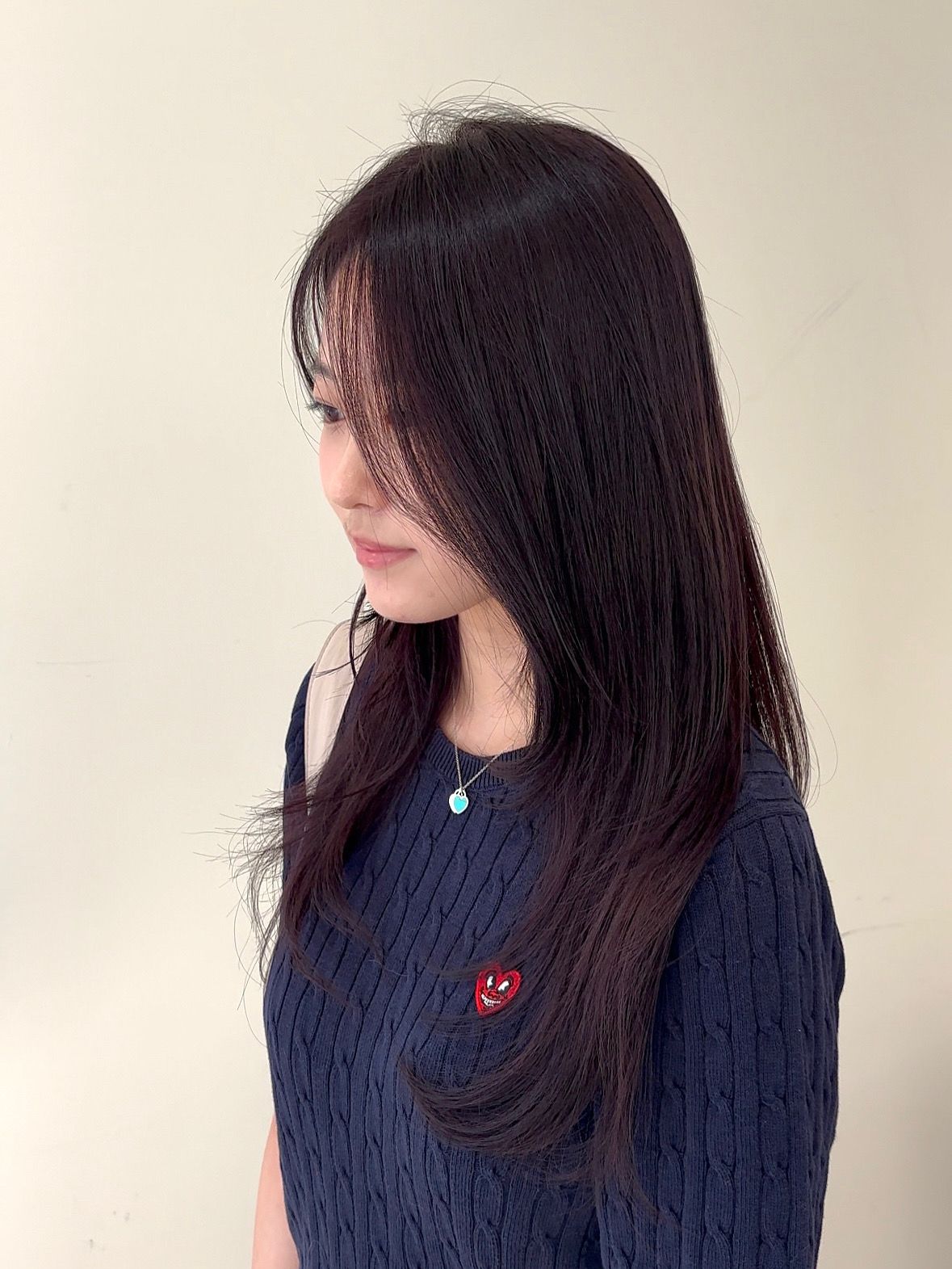 Side-profile portrait of a woman with long dark hair wearing a navy sweater and turquoise pendant.