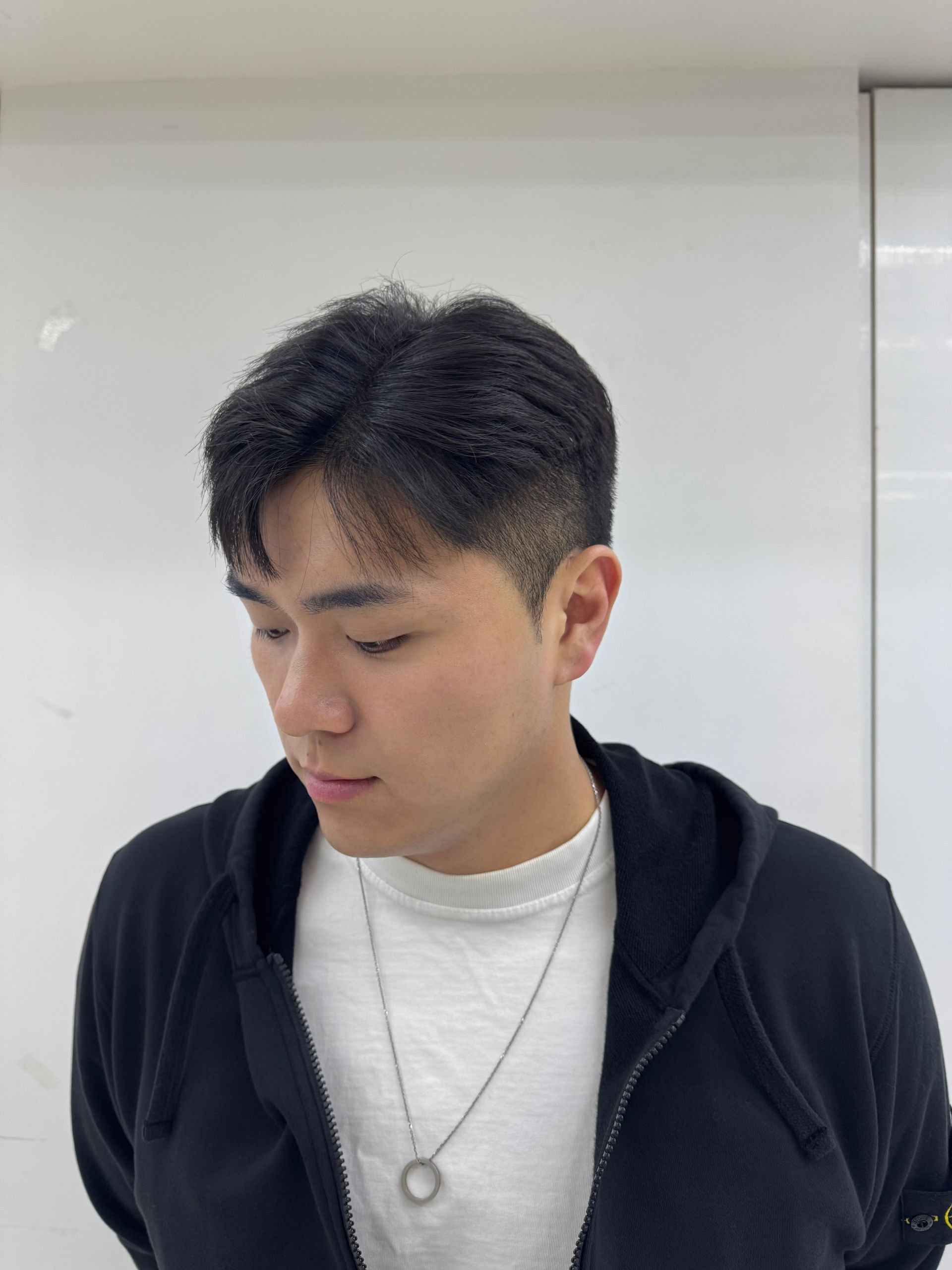 Person in a black hoodie and white shirt looking down in front of a whiteboard.