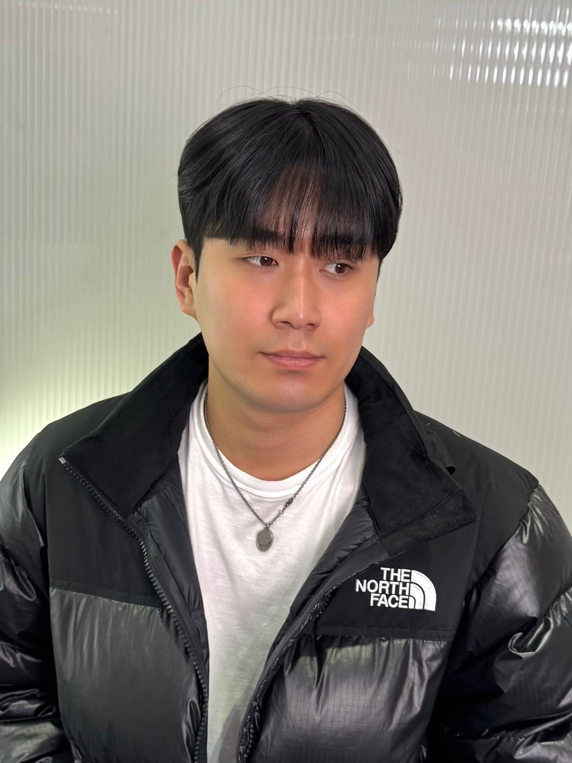 Young person in a black North Face jacket and white shirt, looking slightly to the side against a light backdrop