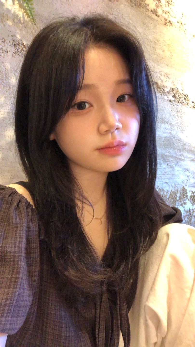 Portrait of a person with long dark hair wearing a brown top, looking at the camera indoors.