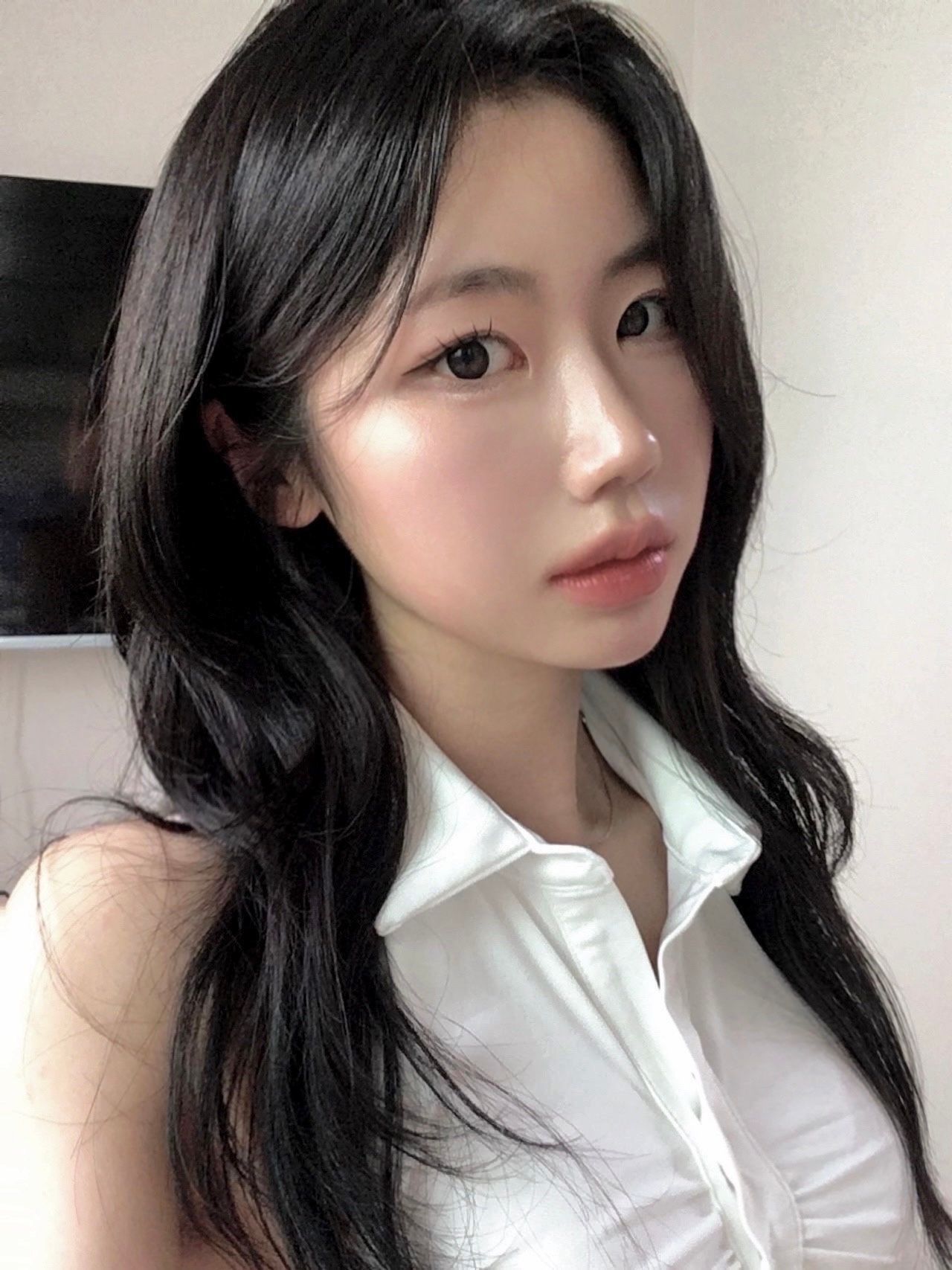 Portrait of a woman with long black hair wearing a white sleeveless blouse against a light background