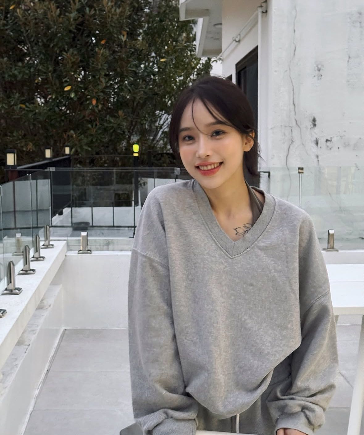 Smiling woman in a gray sweatshirt sitting outdoors on a rooftop terrace