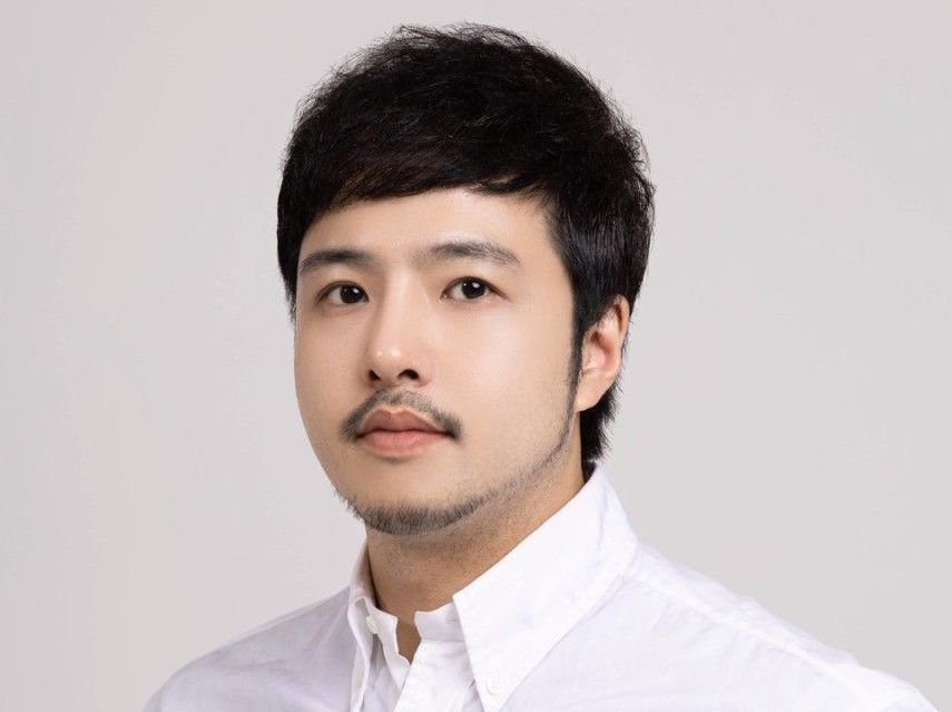 Portrait of a man with short dark hair and a mustache, wearing a white shirt against a light background