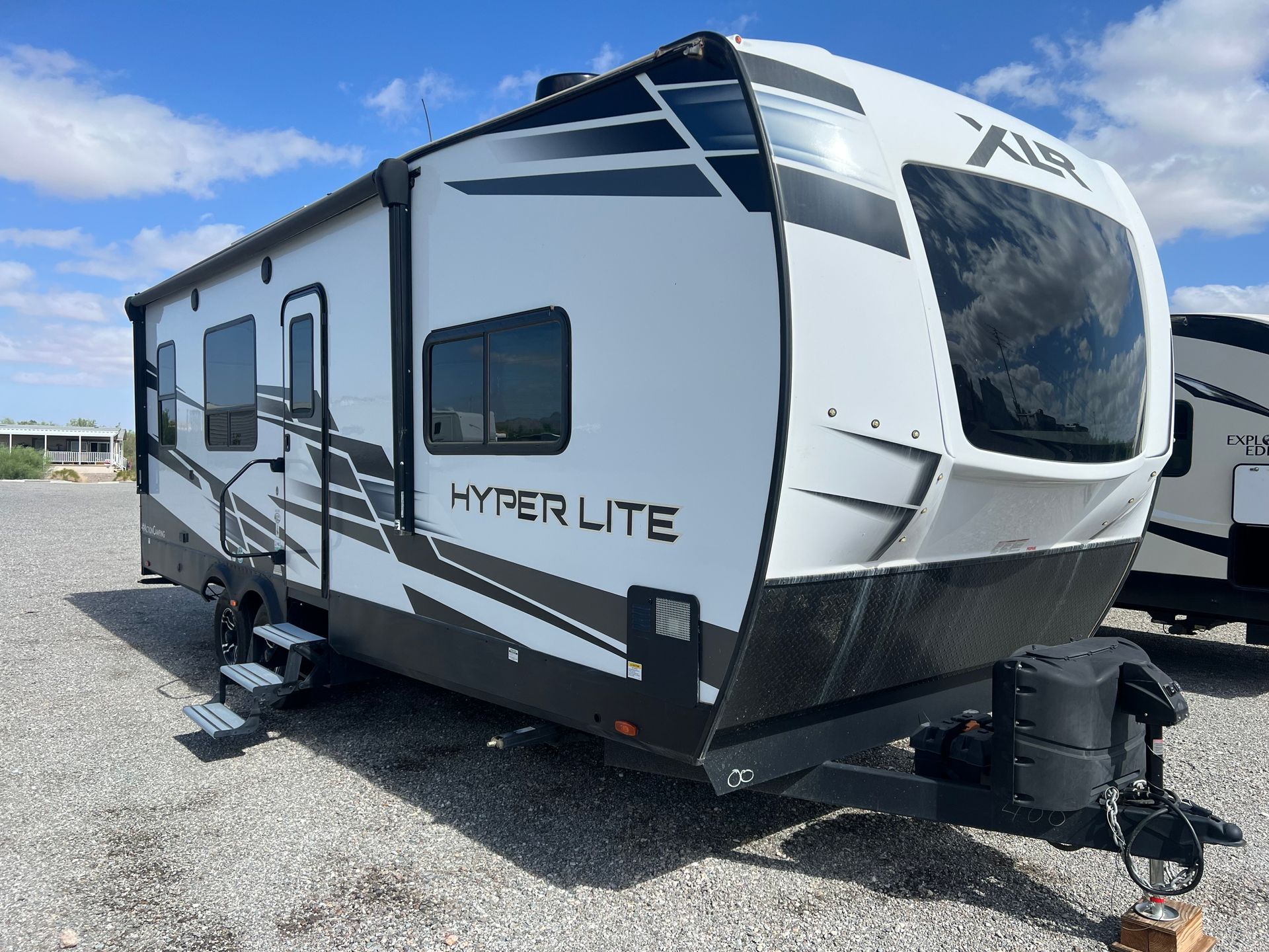 White and black travel trailer labeled "Hyper Lite" on a gravel lot under a cloudy sky.