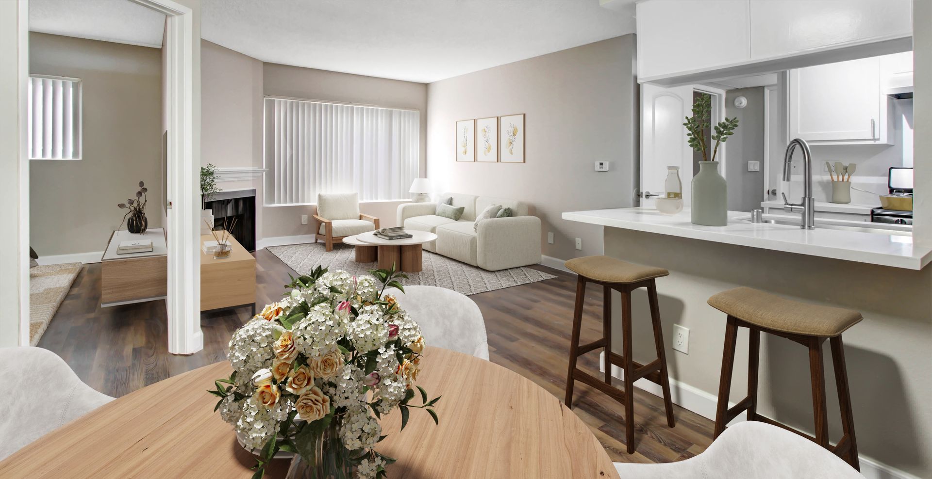 A sunlit, open-concept living area with a dining table, kitchen island with stools, and a cozy lounge space.