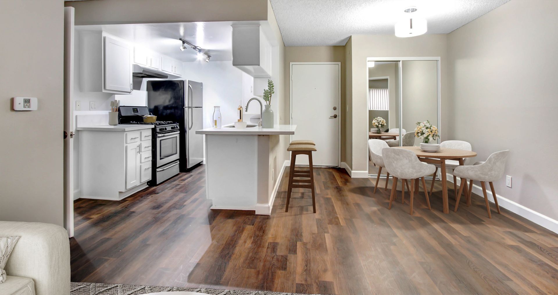 Open-plan kitchen and dining area with wood floors, white walls, and a small round table by the window.