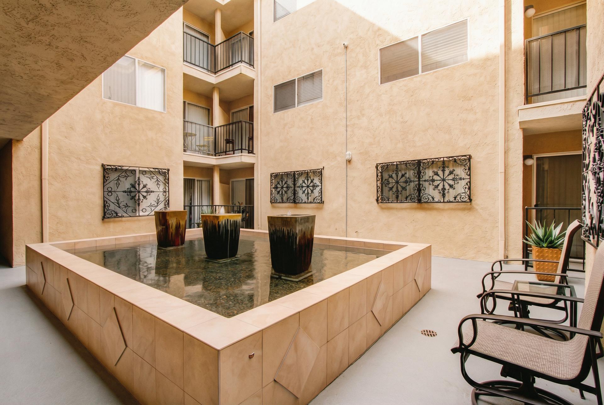 Courtyard with a central fountain, beige apartment walls, and wrought-iron chairs