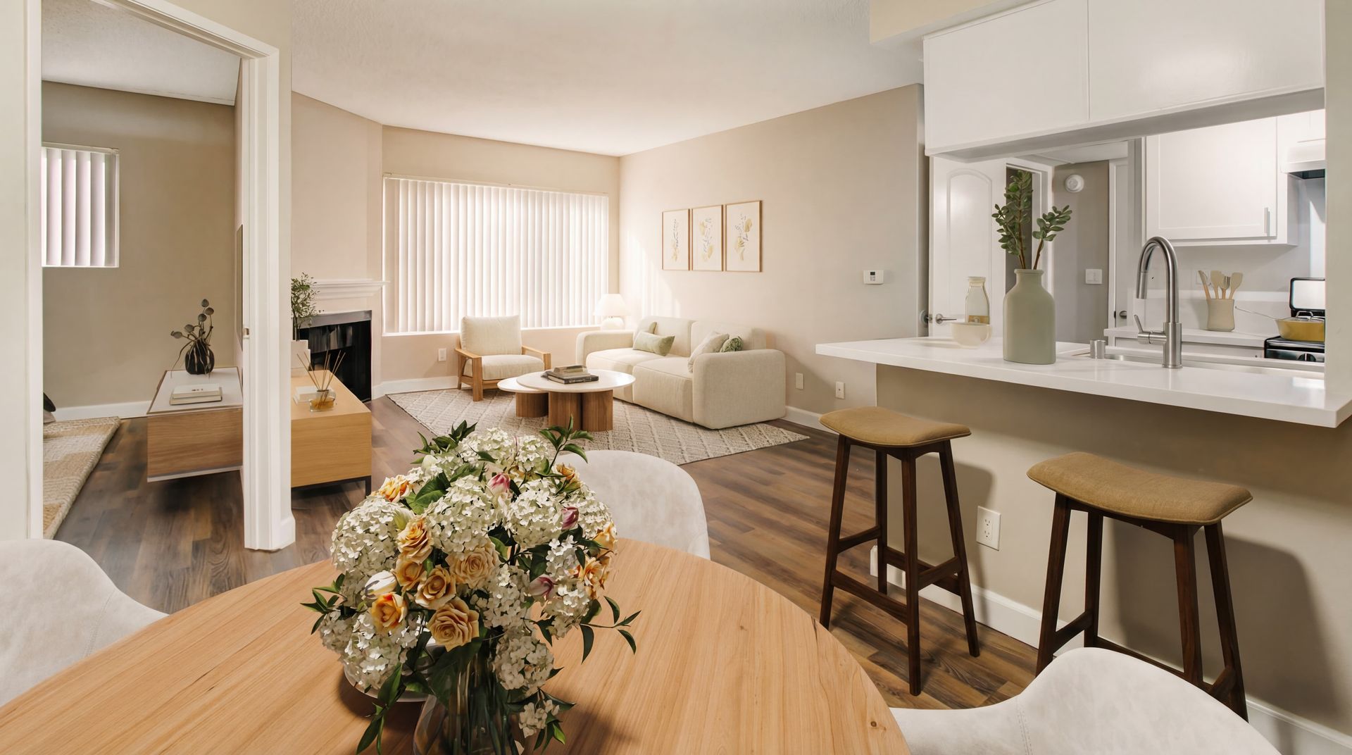 A sunlit, open-concept living area with a dining table, kitchen island with stools, and a cozy lounge space.