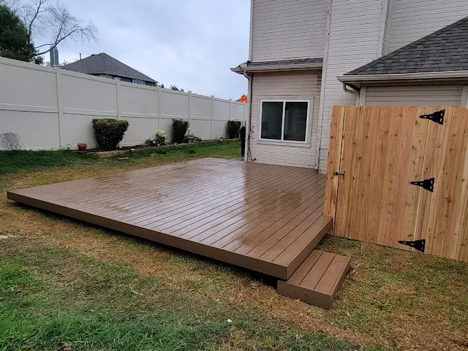 Wooden deck and small steps in a grassy backyard next to a house and a wooden fence.