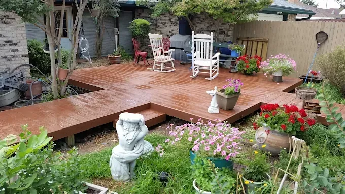Outdoor wooden deck with rocking chairs, surrounded by flowers and greenery.