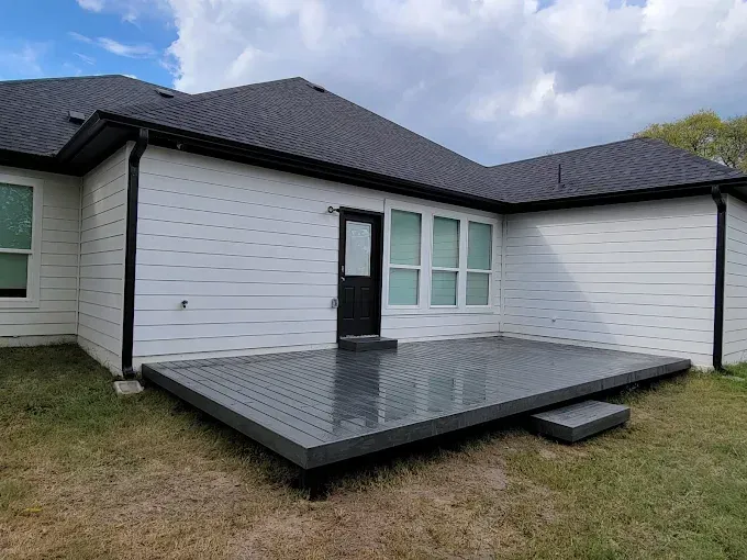 Backyard with a gray composite deck, leading to a black door, and white house.
