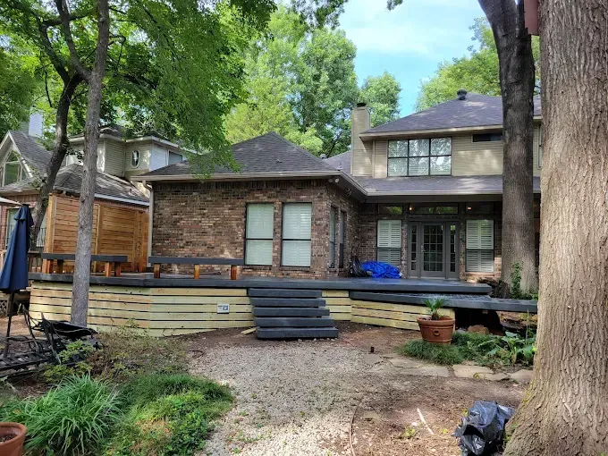 Backyard view of a brick home with a multi-level deck, trees, and grass.