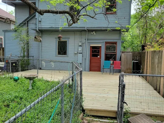 Backyard with wooden deck, blue house, red door, two chairs, green lawn, and wire fence.