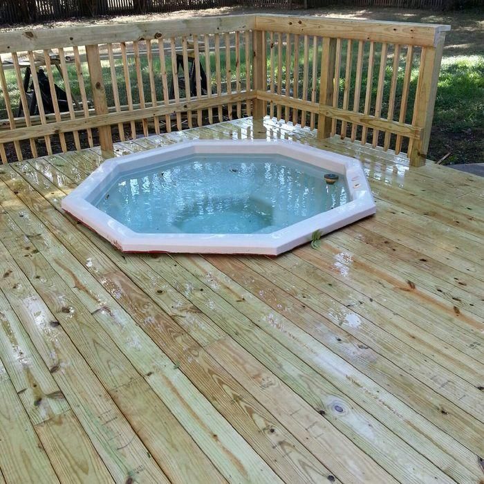 Wooden deck with an octagonal hot tub surrounded by a railing, outdoors.