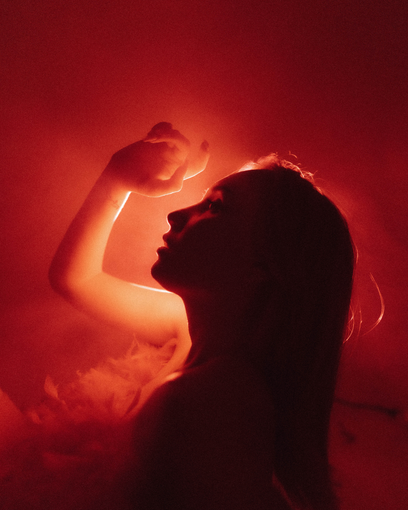 Silhouette of a person with an arm raised. Illuminated in red light, possibly smoke.