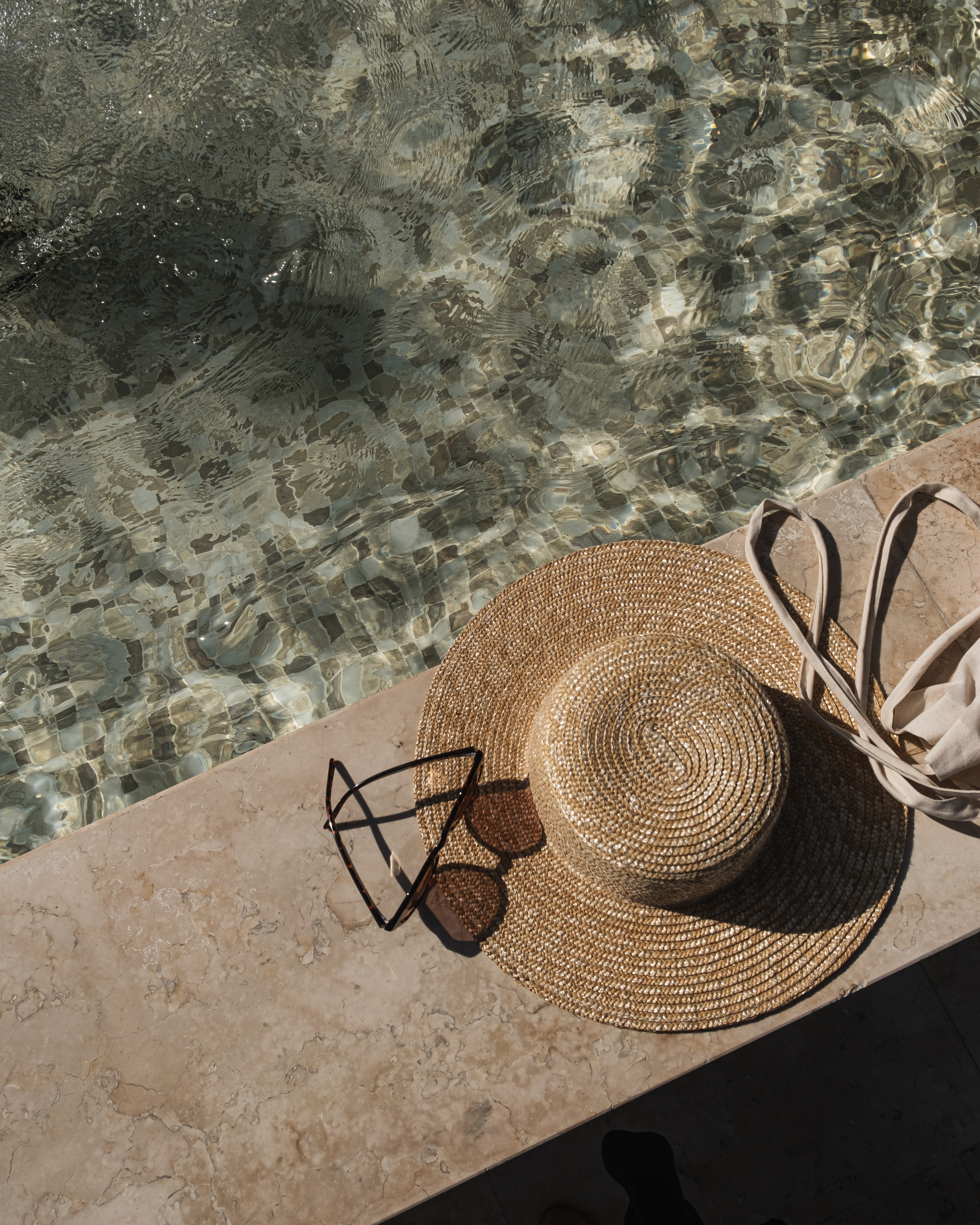 Sun hat, sunglasses, and tote bag by a pool.