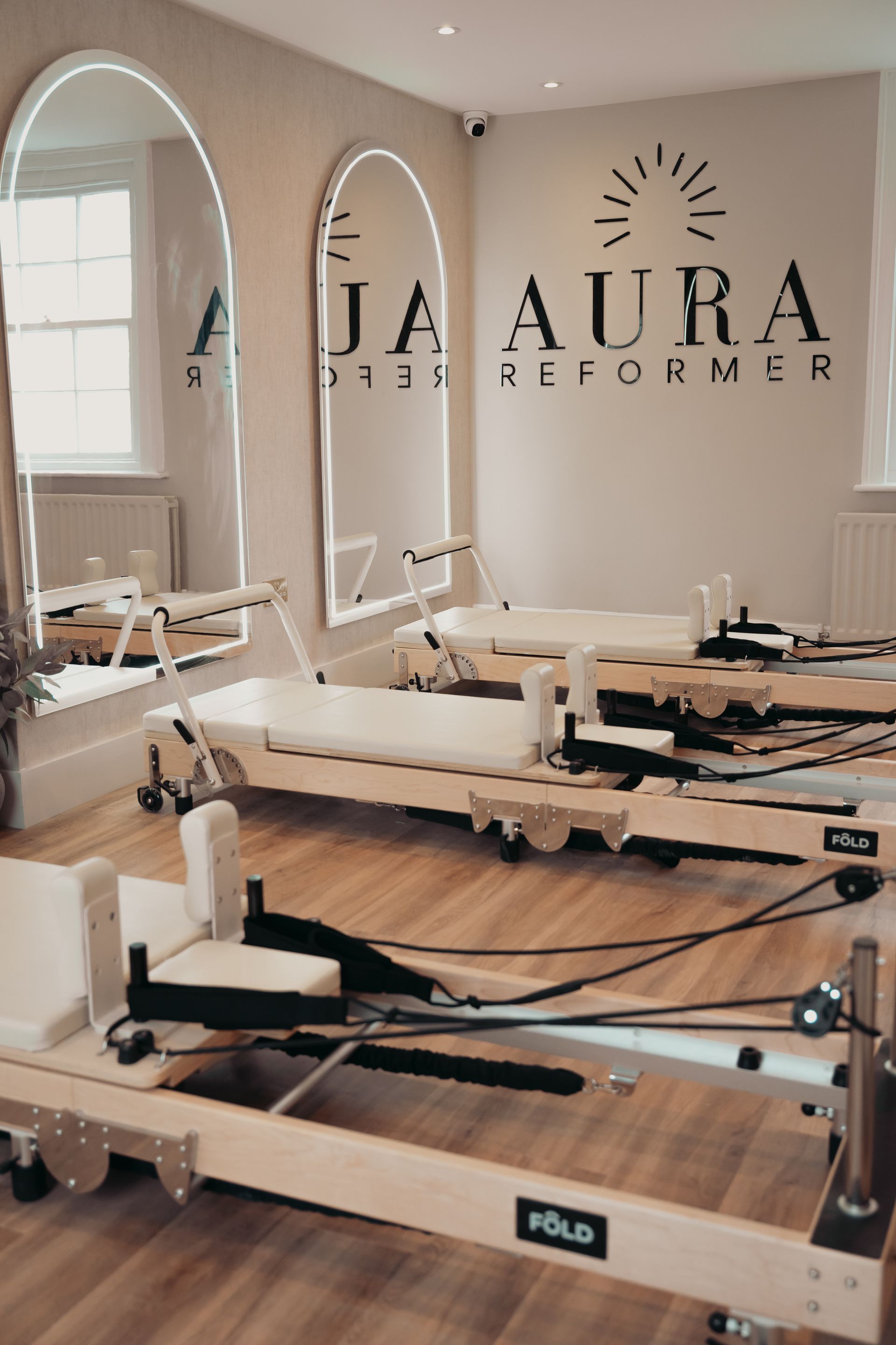 Woman in workout clothes using a pilates machine, kneeled position, arm extended with strap.