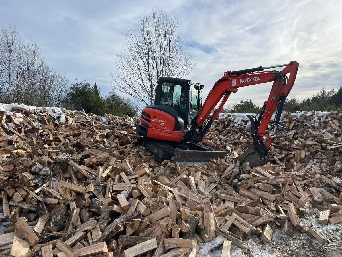 A red excavator is sitting on top of a pile of wood.