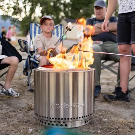 A group of people are sitting around a fire pit roasting marshmallows.