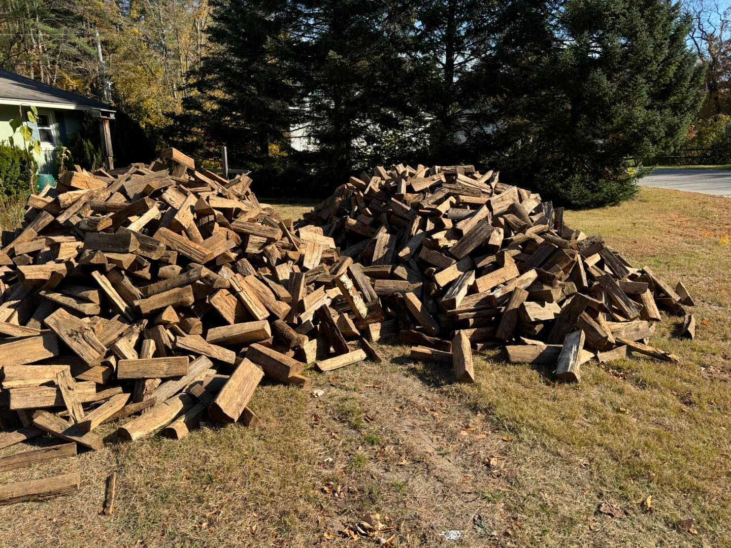 A pile of wood is sitting in the grass in front of a house.