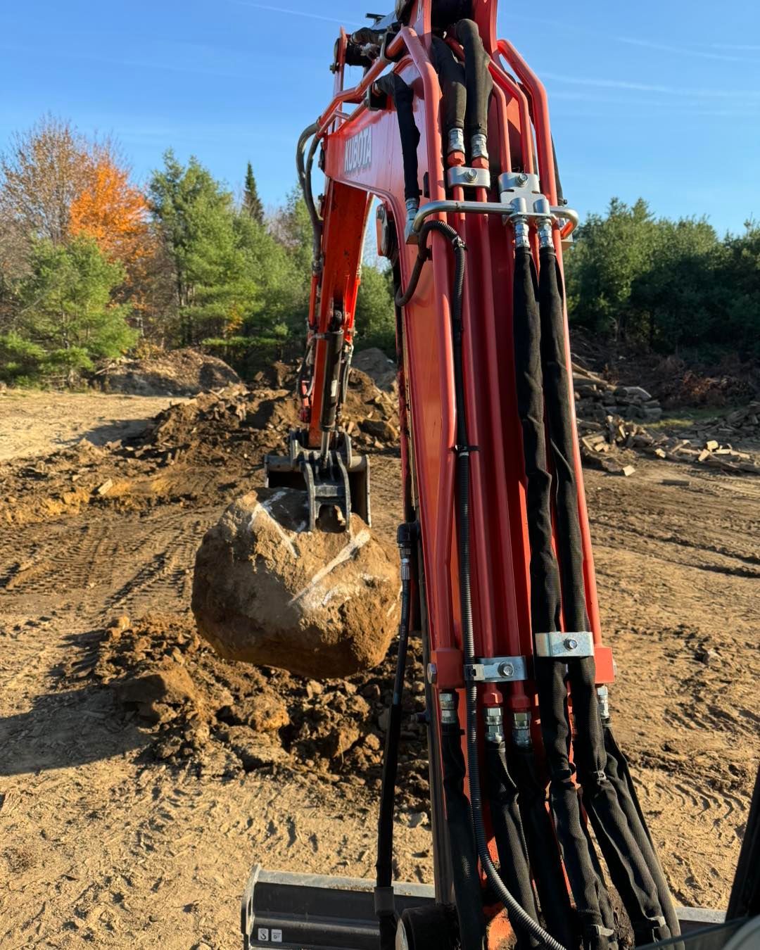 A red excavator is carrying a large rock in its bucket.