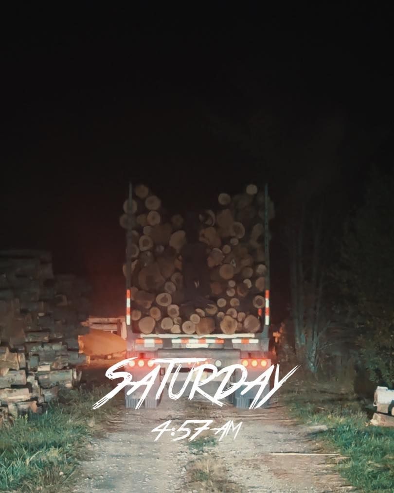 A truck filled with logs is driving down a dirt road at night.