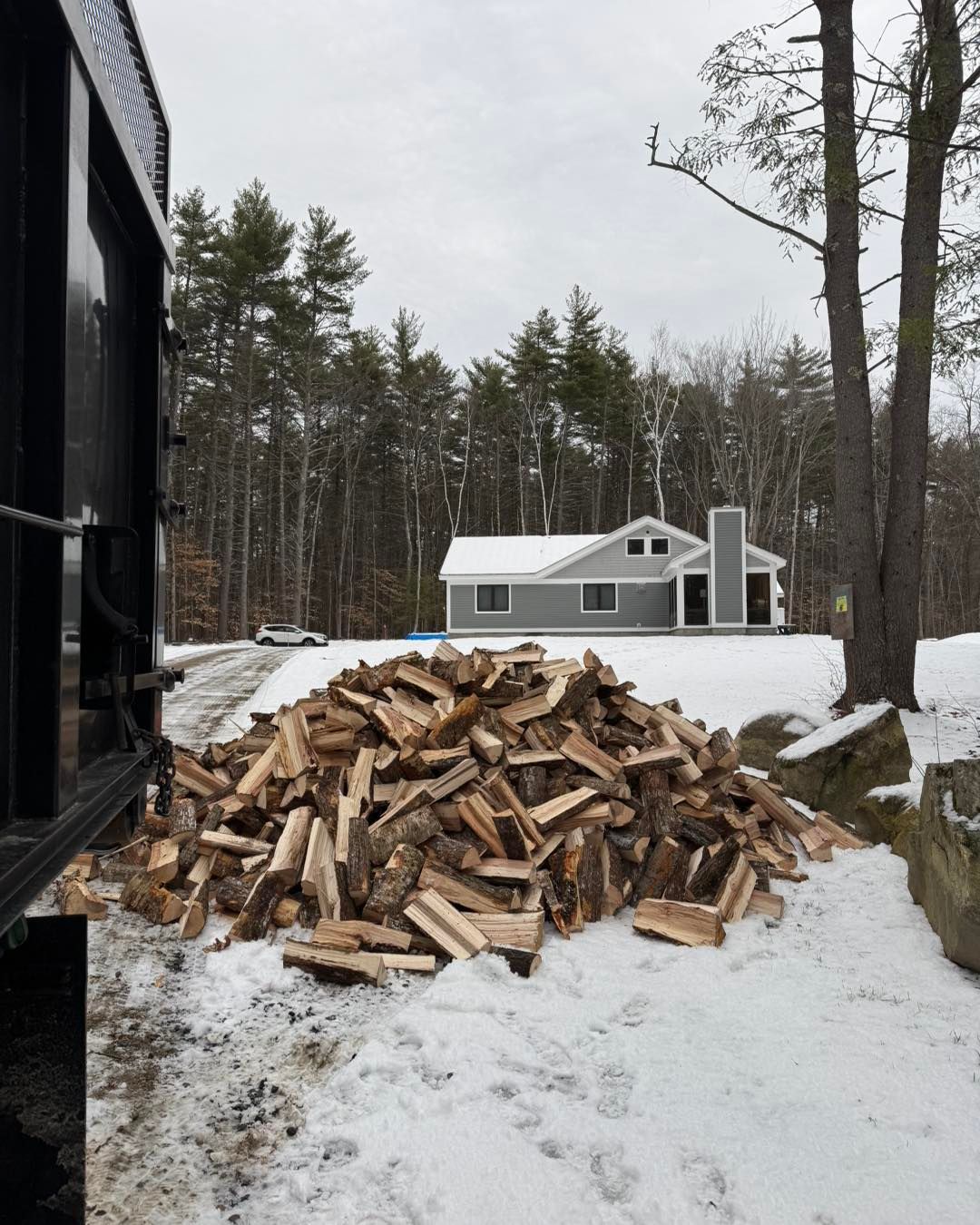 A pile of wood in the snow with a house in the background