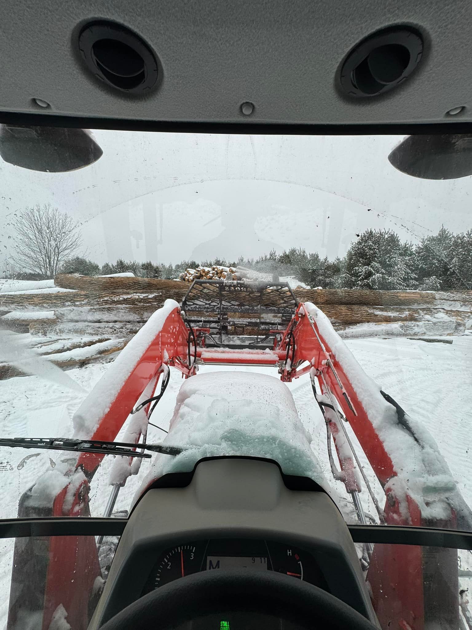 A red tractor is driving through a snowy field.