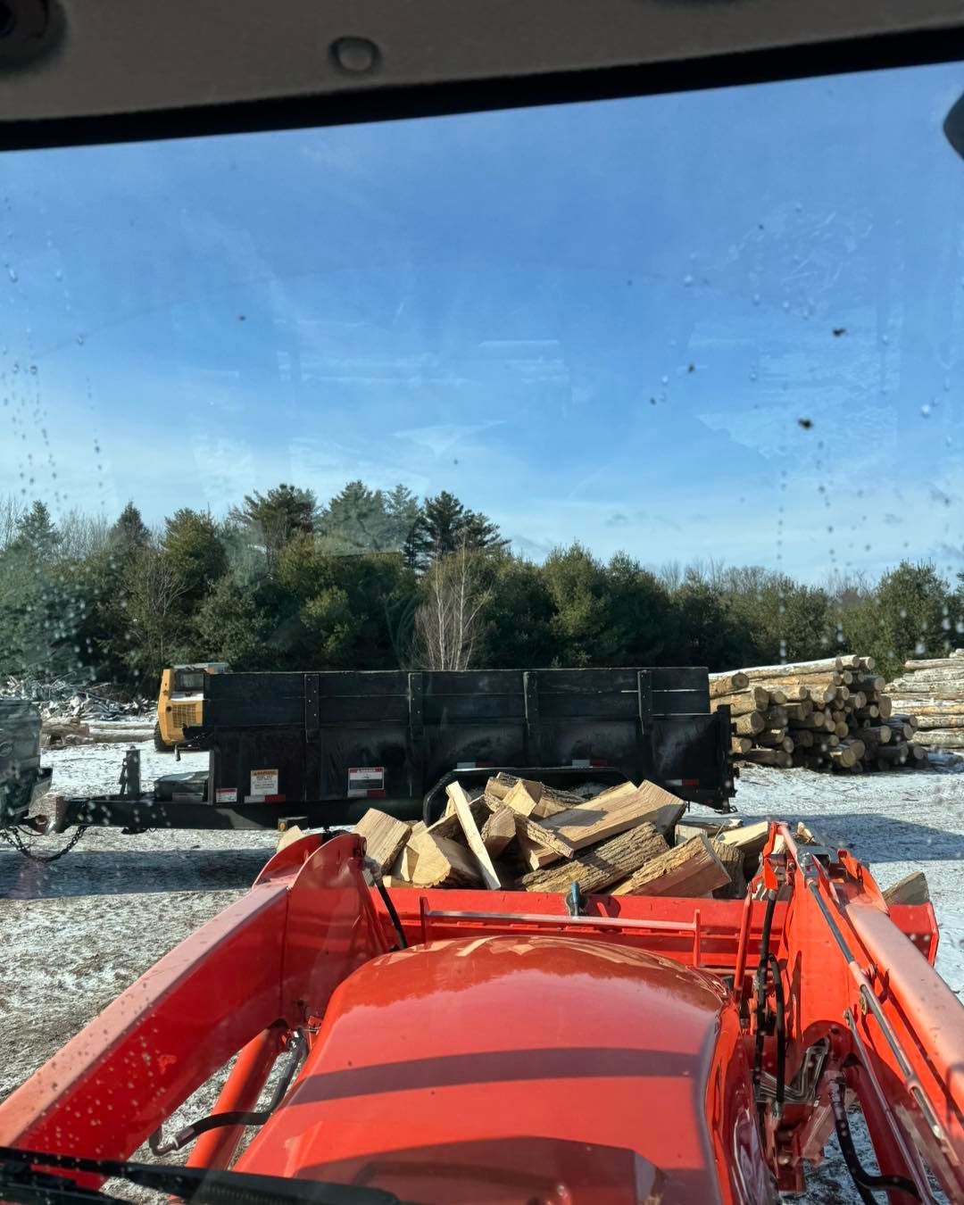 A red tractor is parked in front of a pile of logs.