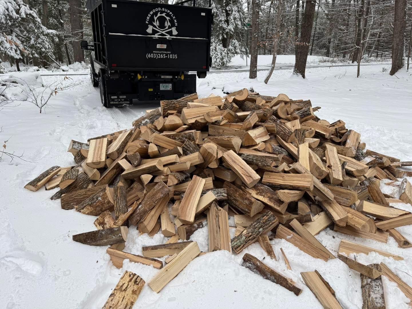 A pile of wood is sitting in the snow next to a dump truck.
