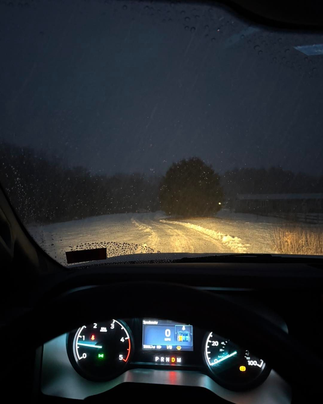 A car is driving down a snowy road at night