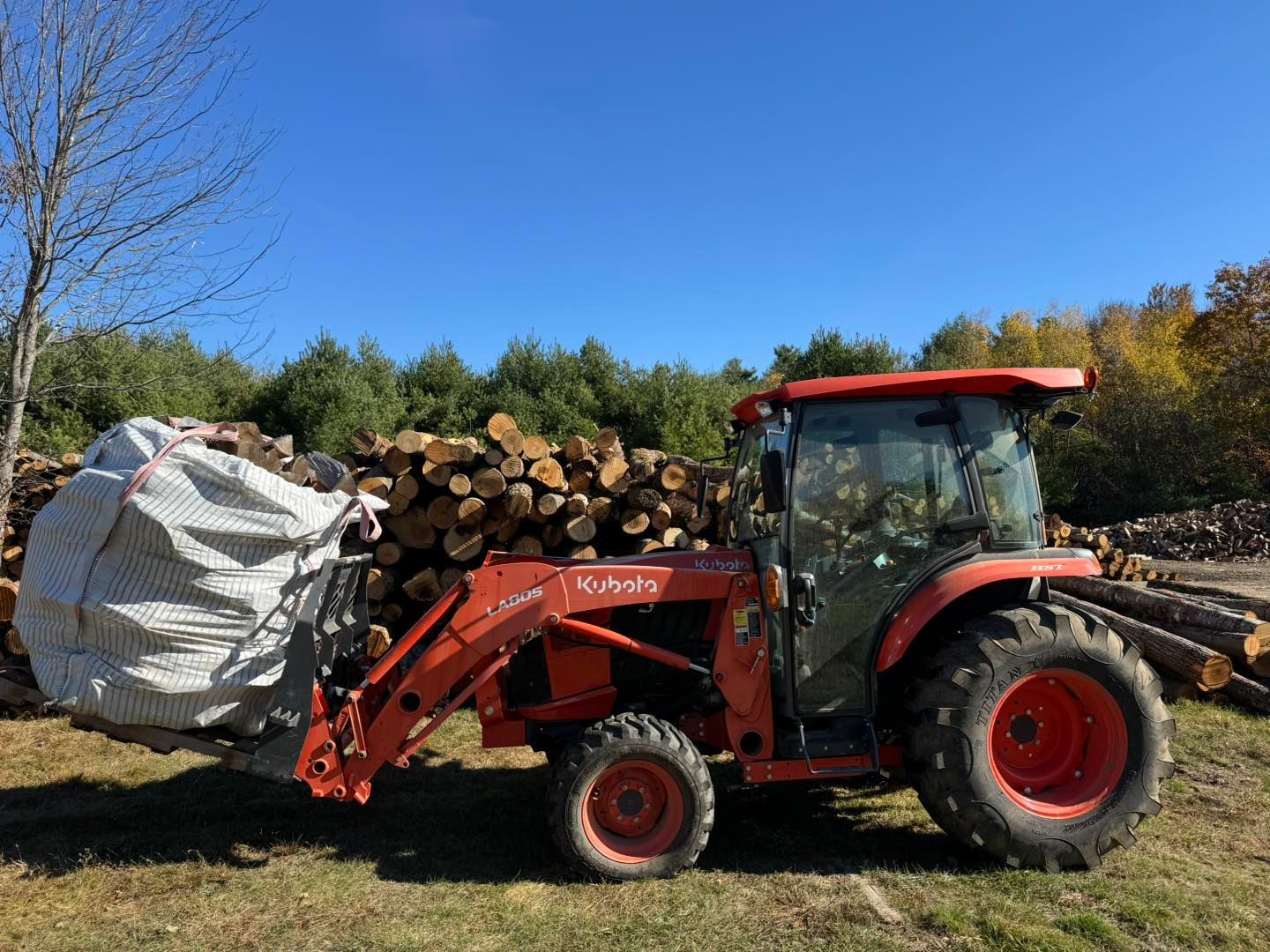 A red tractor is carrying a bag of logs in a field.