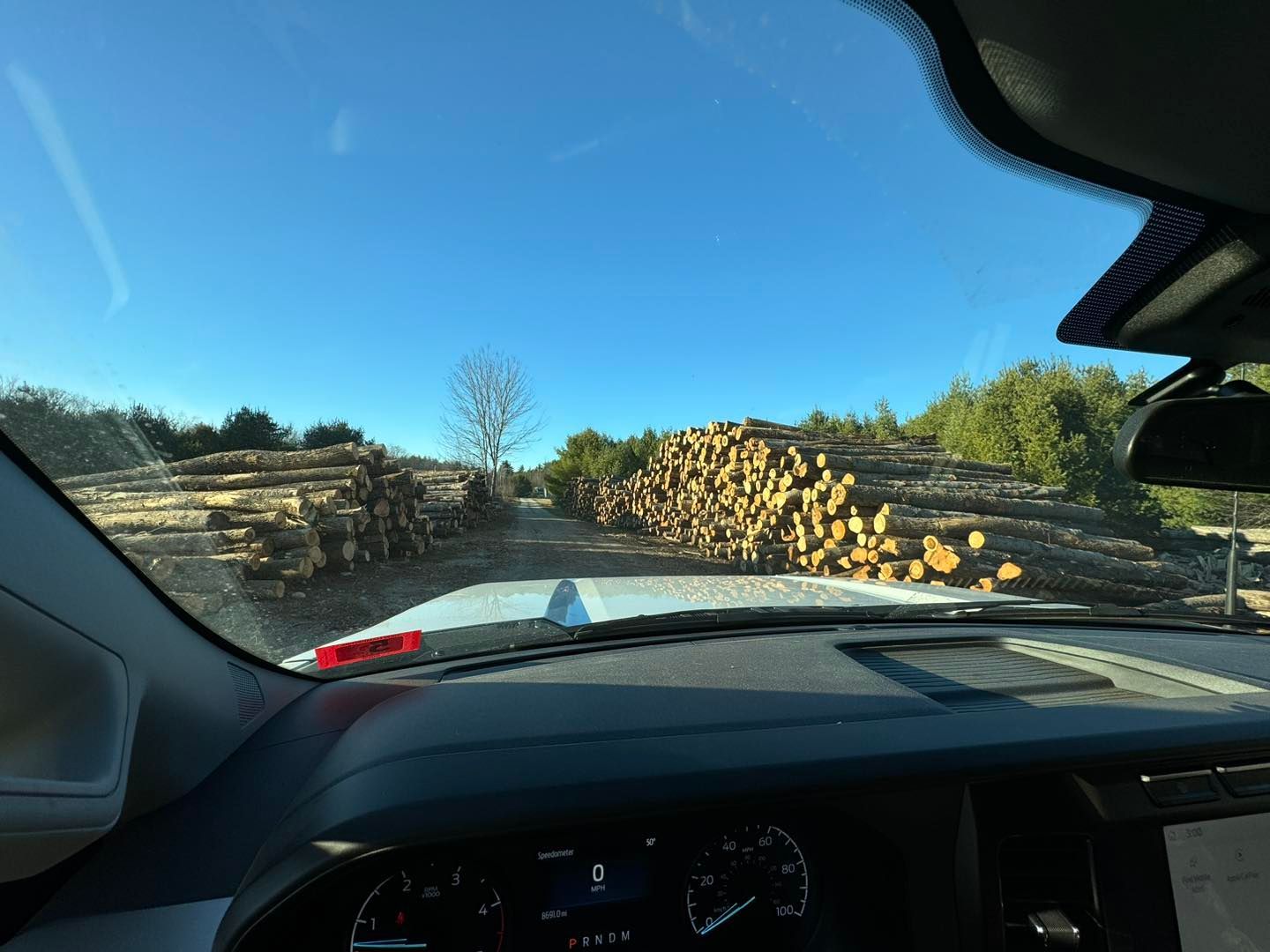 A car is driving down a road next to a pile of logs.