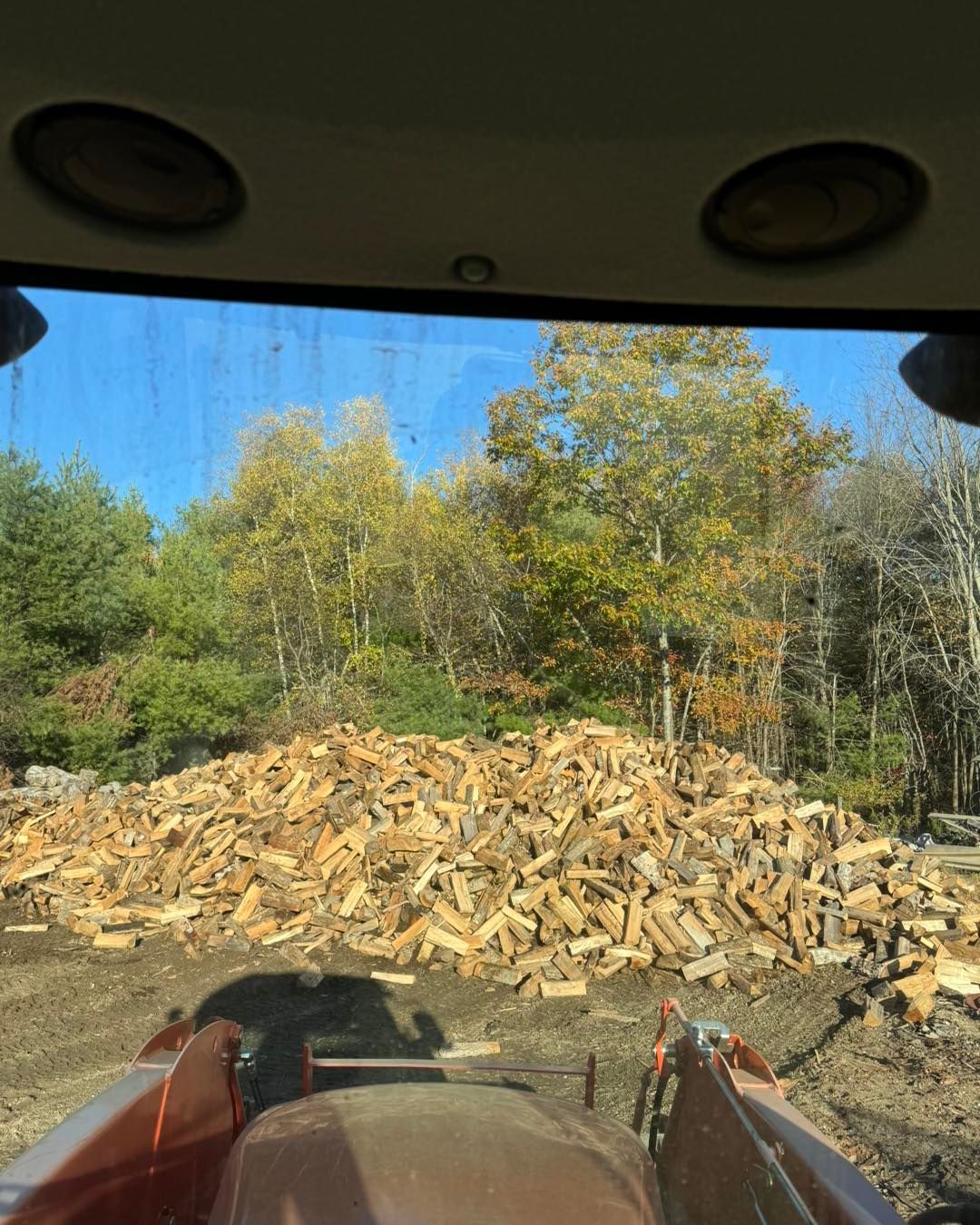 A tractor is driving down a dirt road next to a pile of wood.