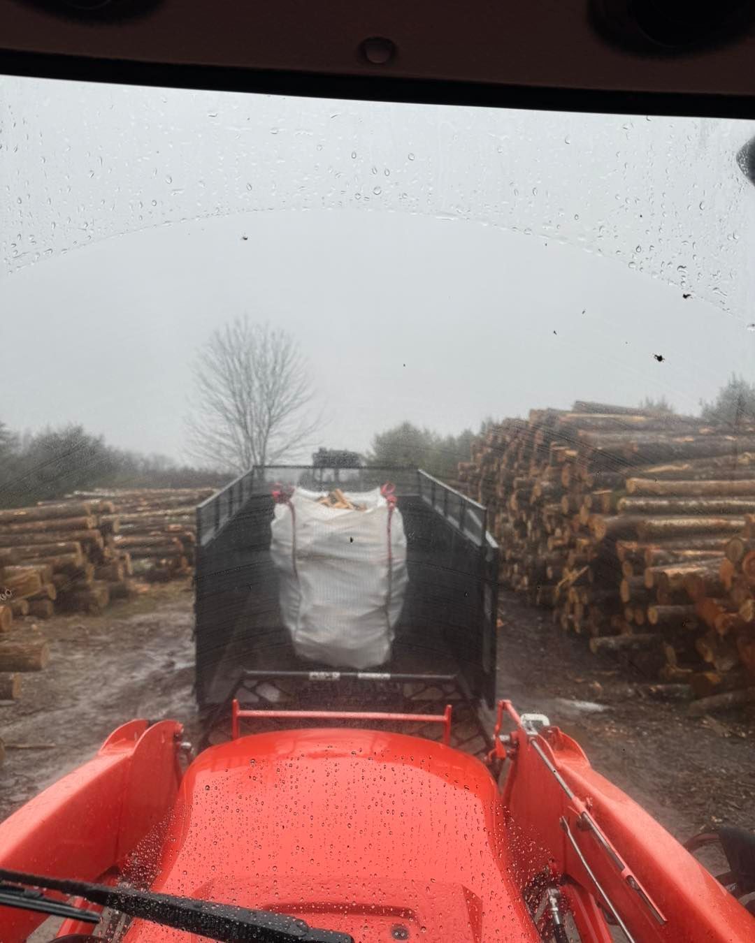 A red tractor is driving through a field of logs.