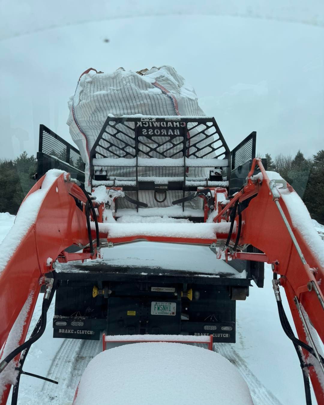 A large rock is being lifted by a tractor in the snow.