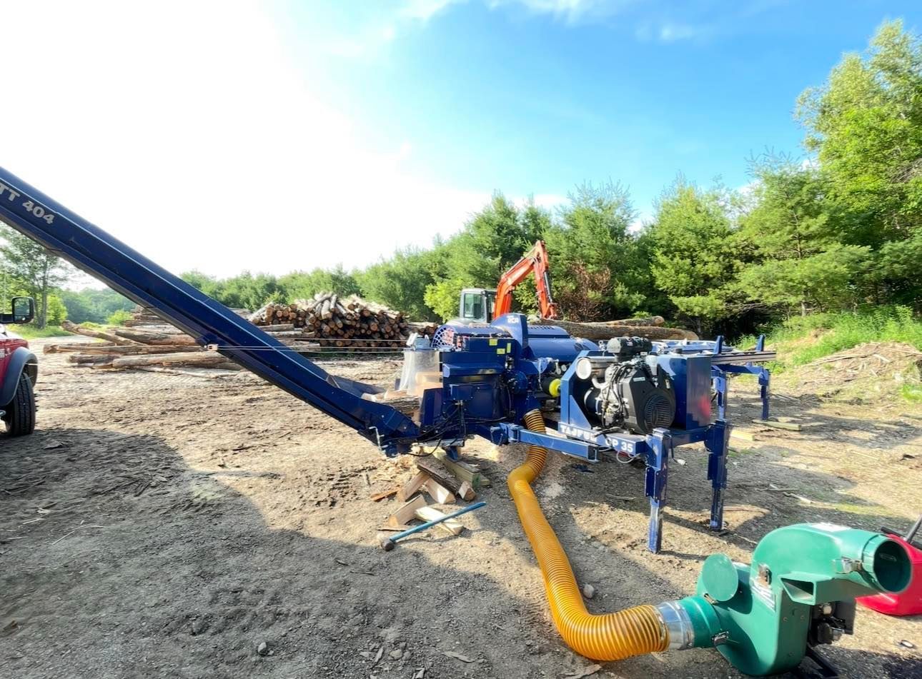 A machine is sitting in a dirt field next to a pile of logs.